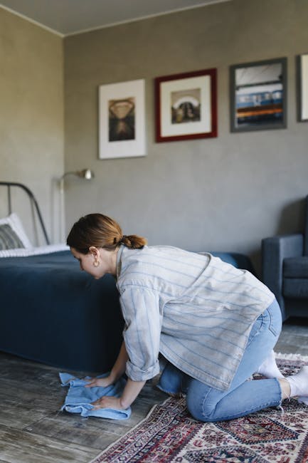 A person kneeling on a patterned carpet in a residential setting, using a black and yellow vacuum cleaner for surface cleaning. Their hands are inserting a white cloth into the vacuum's dust compartme