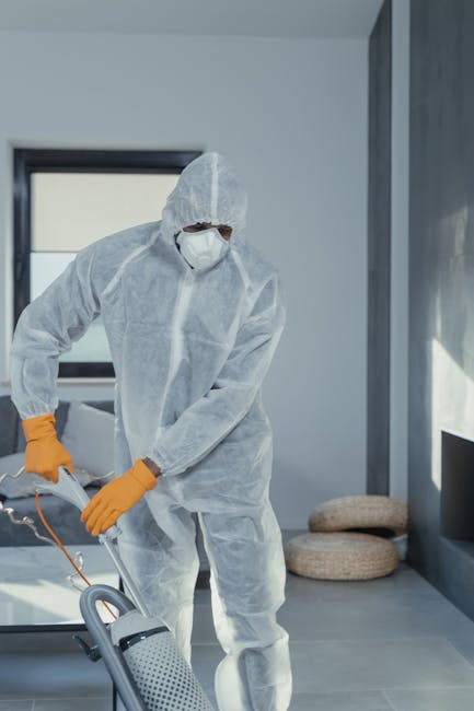 A person is using a yellow portable vacuum cleaner with a black hose to clean a patterned area rug in a residential room. The rug features a floral motif in muted tones of beige, green, and orange, situated on a wooden floor. The individual is dressed in casual clothing, including jeans and white sneakers, and is holding the vacuum wand with both hands, focusing on surface cleaning the rug. Bright, natural lighting illuminates the space, highlighting the cleanliness of the rug and surrounding surfaces. Carpet Cleaning Kingston is providing deep cleaning services to ensure hygiene and freshness in the living area.